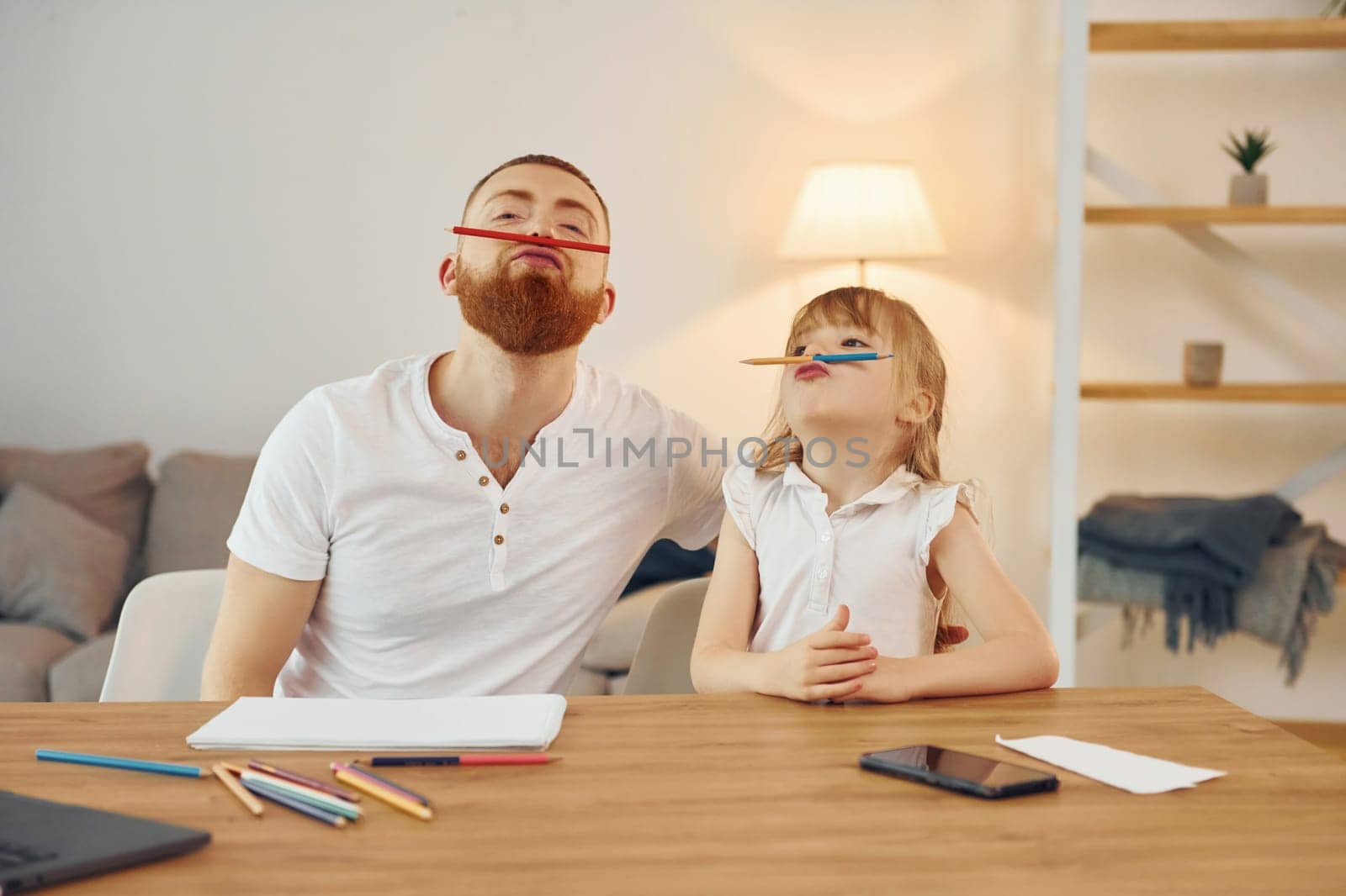 Sitting by the table and having fun. Father with his little daughter is at home together.