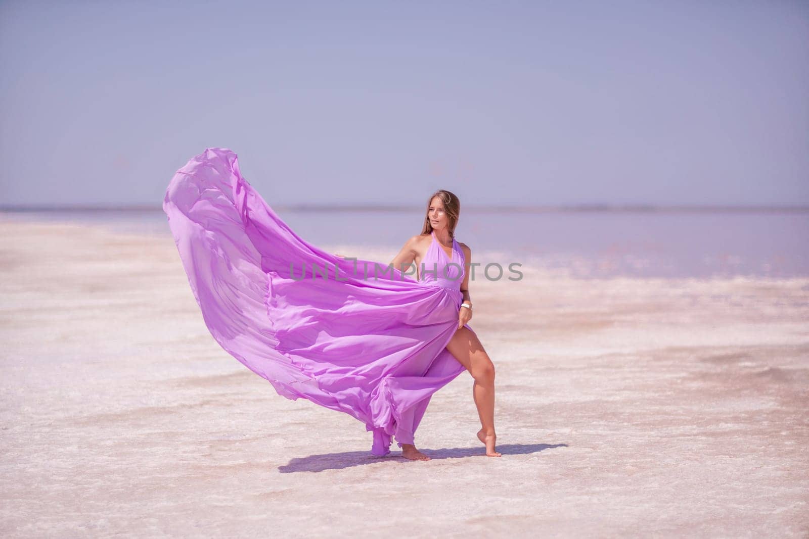 Woman in pink salt lake. She walks in a pink long dress and hat along the salty white shore of the lake. Wanderlust photo for memory.