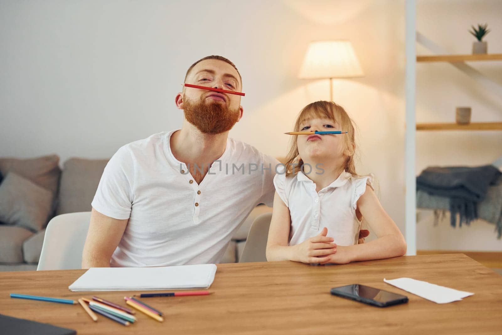 Sitting by the table and having fun. Father with his little daughter is at home together.