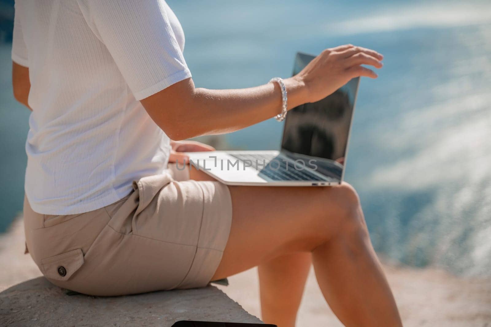 Freelance women sea working on the computer. Good looking middle aged woman typing on a laptop keyboard outdoors with a beautiful sea view. The concept of remote work. by Matiunina