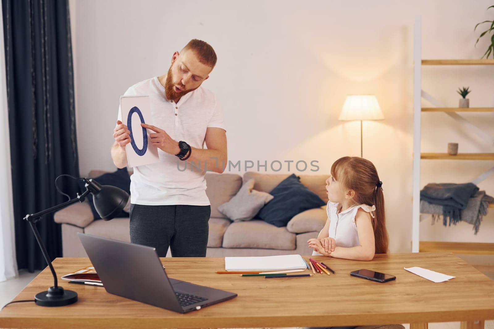 Man shows letters on the paper. Father with his little daughter is at home together.