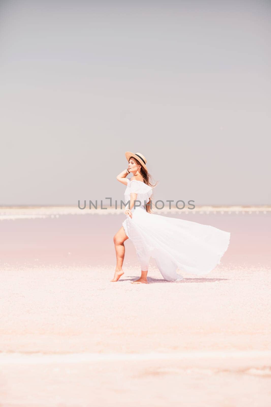 Woman in pink salt lake. She walks in a white long dress and hat along the salty white shore of the lake. Wanderlust photo for memory.