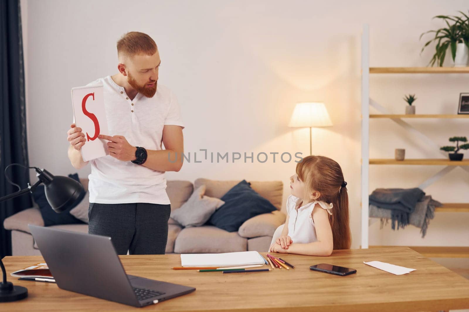 Man shows letters on the paper. Father with his little daughter is at home together.