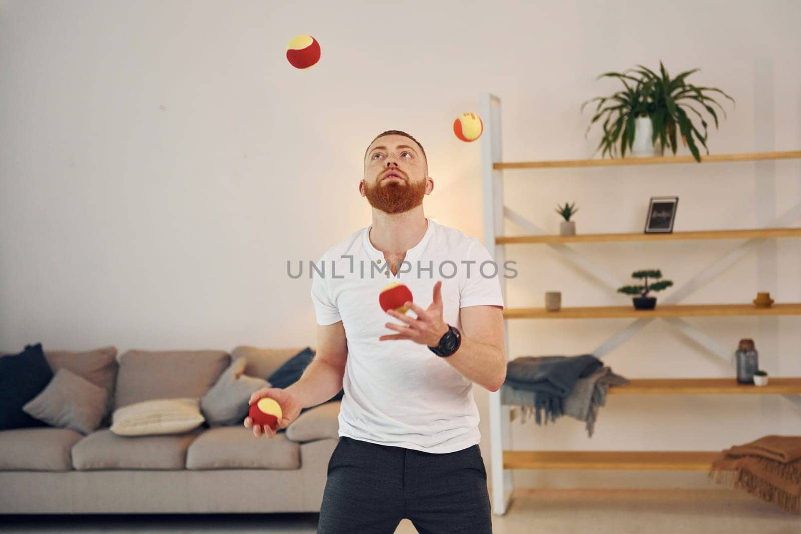 A man in casual clothes throws balls at home.