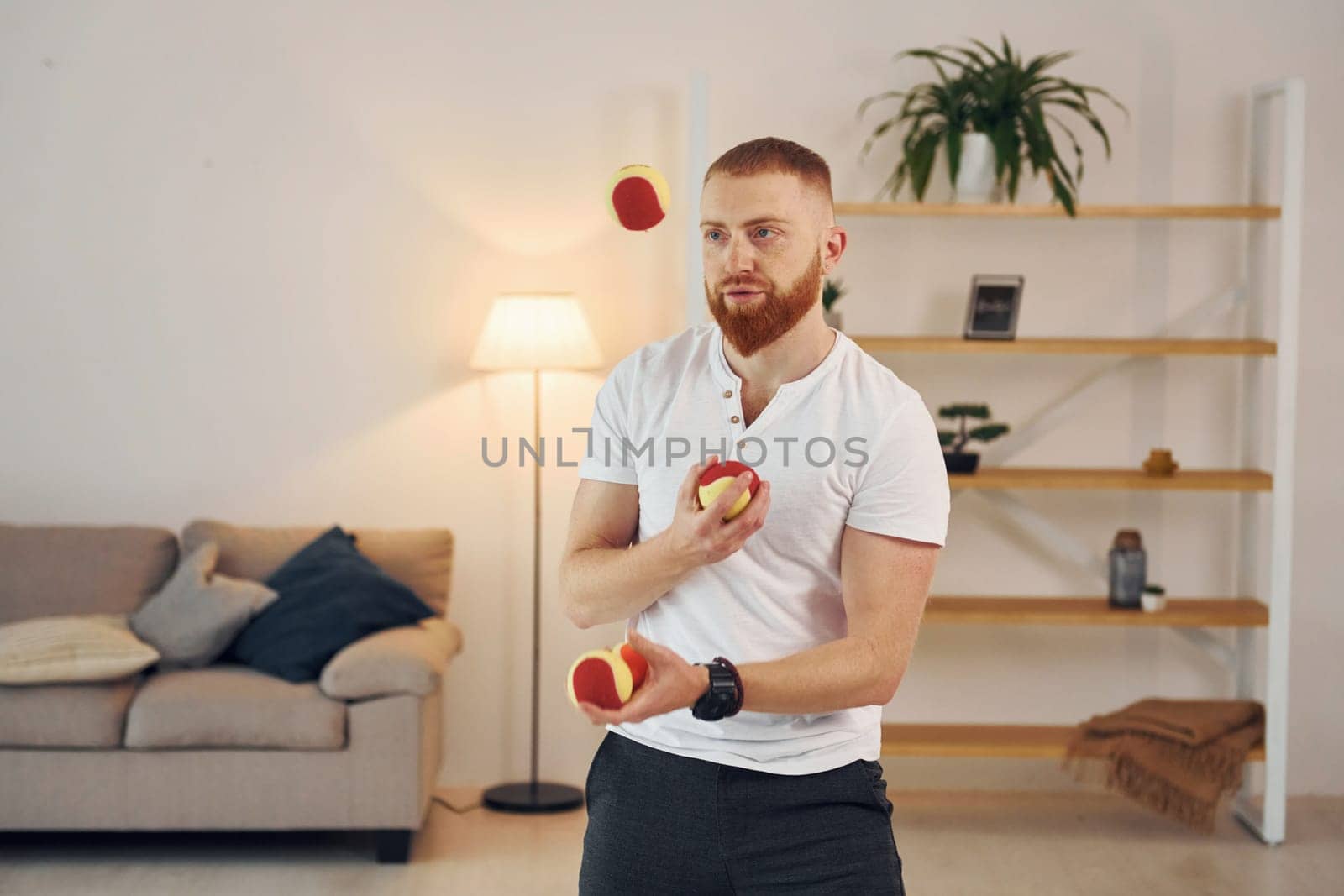 A man in casual clothes throws balls at home.