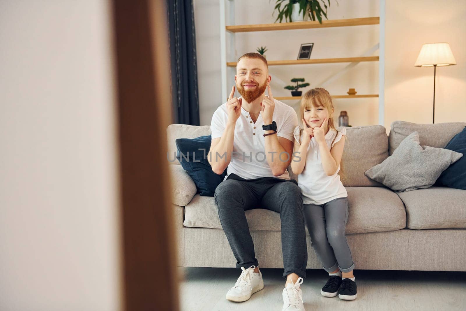 On the sofa. Having fun. Father with his little daughter is at home together.