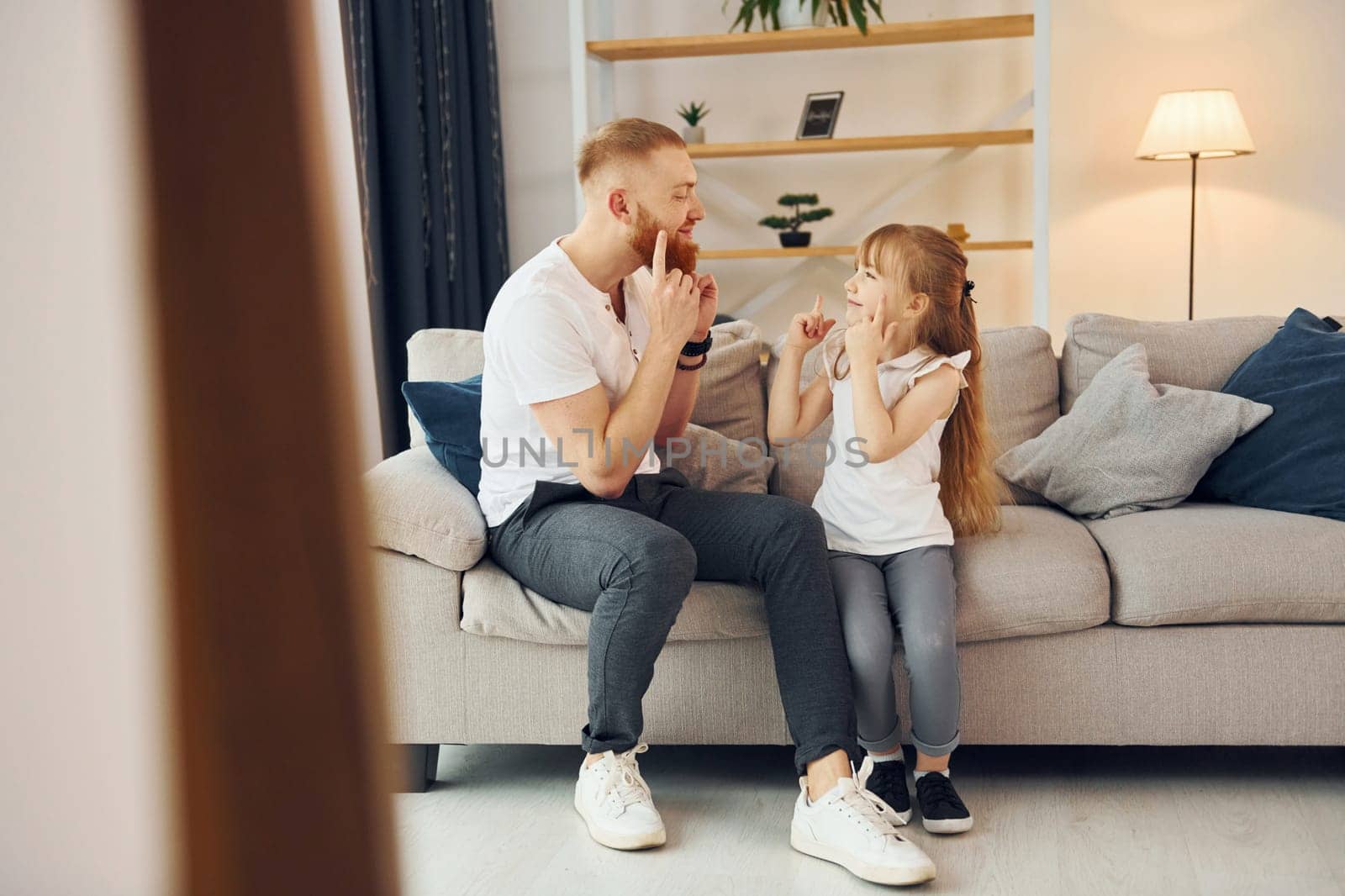 On the sofa. Having fun. Father with his little daughter is at home together.