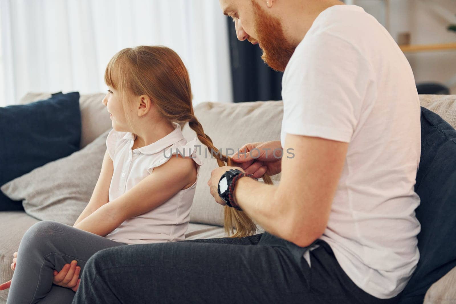 On the sofa. Having fun. Father with his little daughter is at home together.