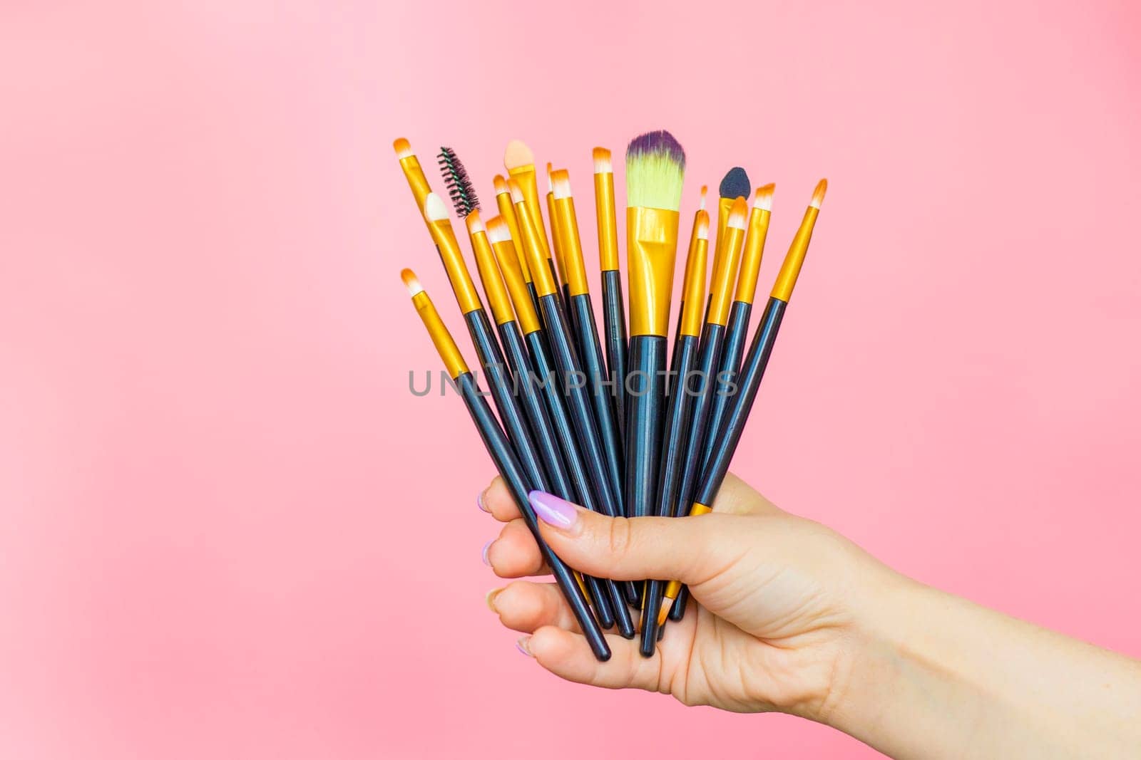 hand holding 15 Makeup Brushes Set, on pink background. beauty cosmetic product layout. woman Stylish design background. Creative fashion concept. Cosmetics make-up collection. makeup artist tools