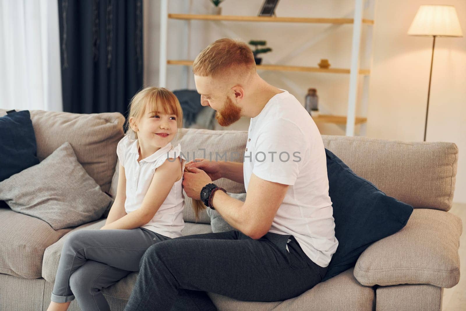 Man braids the braids. Father with his little daughter is at home together.
