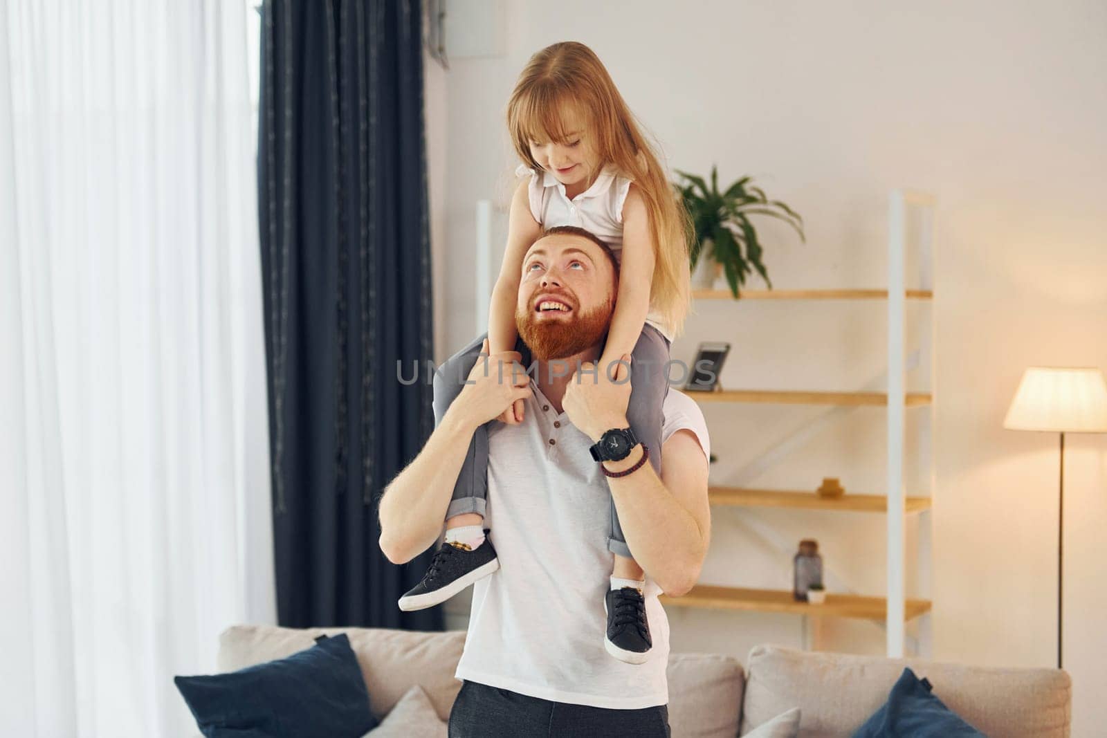 Girl sitting on the shoulders. Father with his little daughter is at home together.