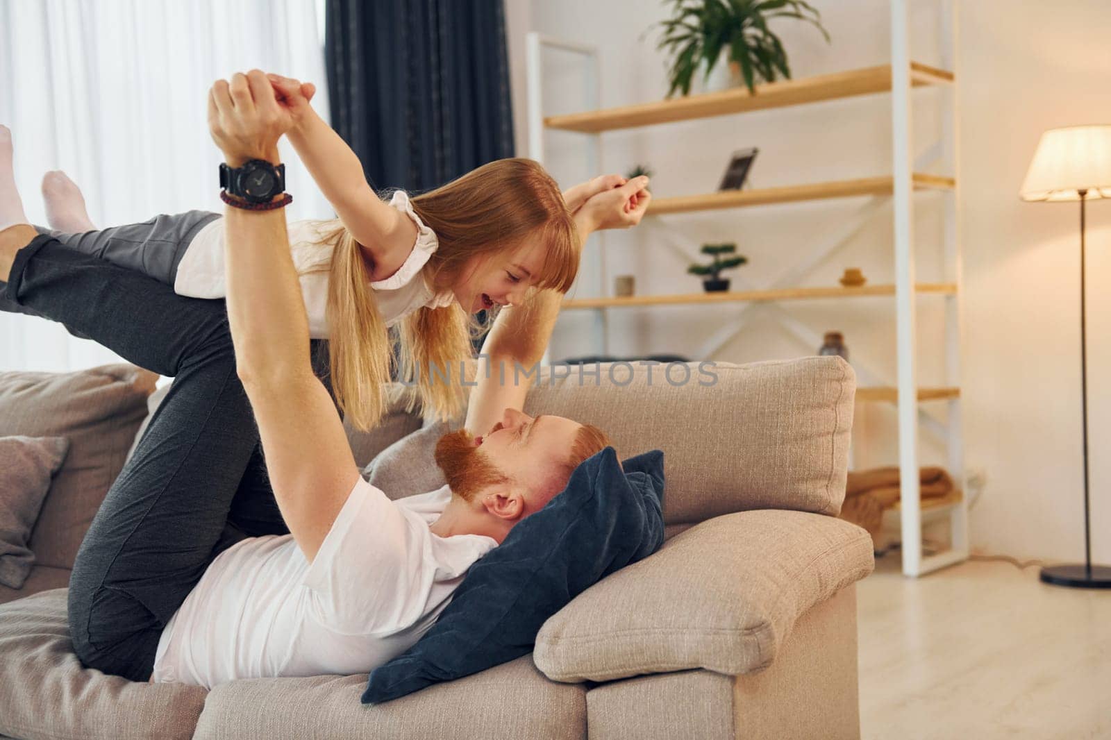 Laying down on the sofa. Father with his little daughter is at home together.
