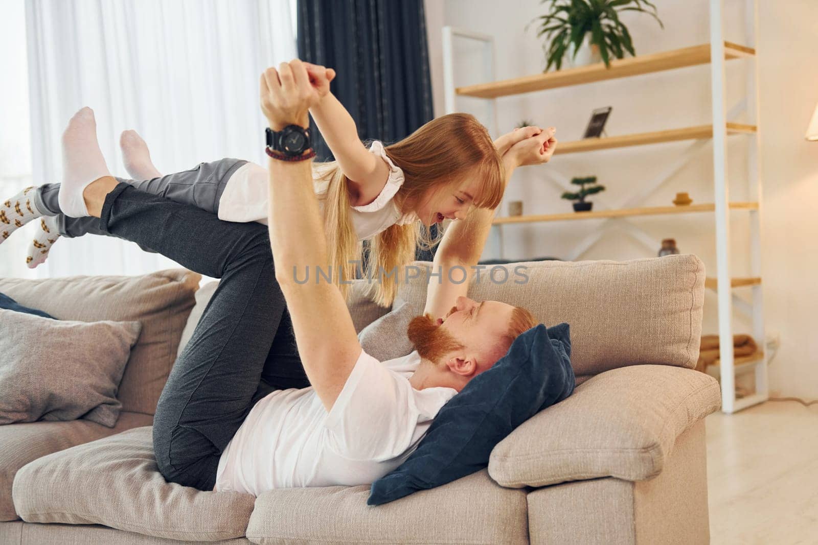 Laying down on the sofa. Father with his little daughter is at home together.