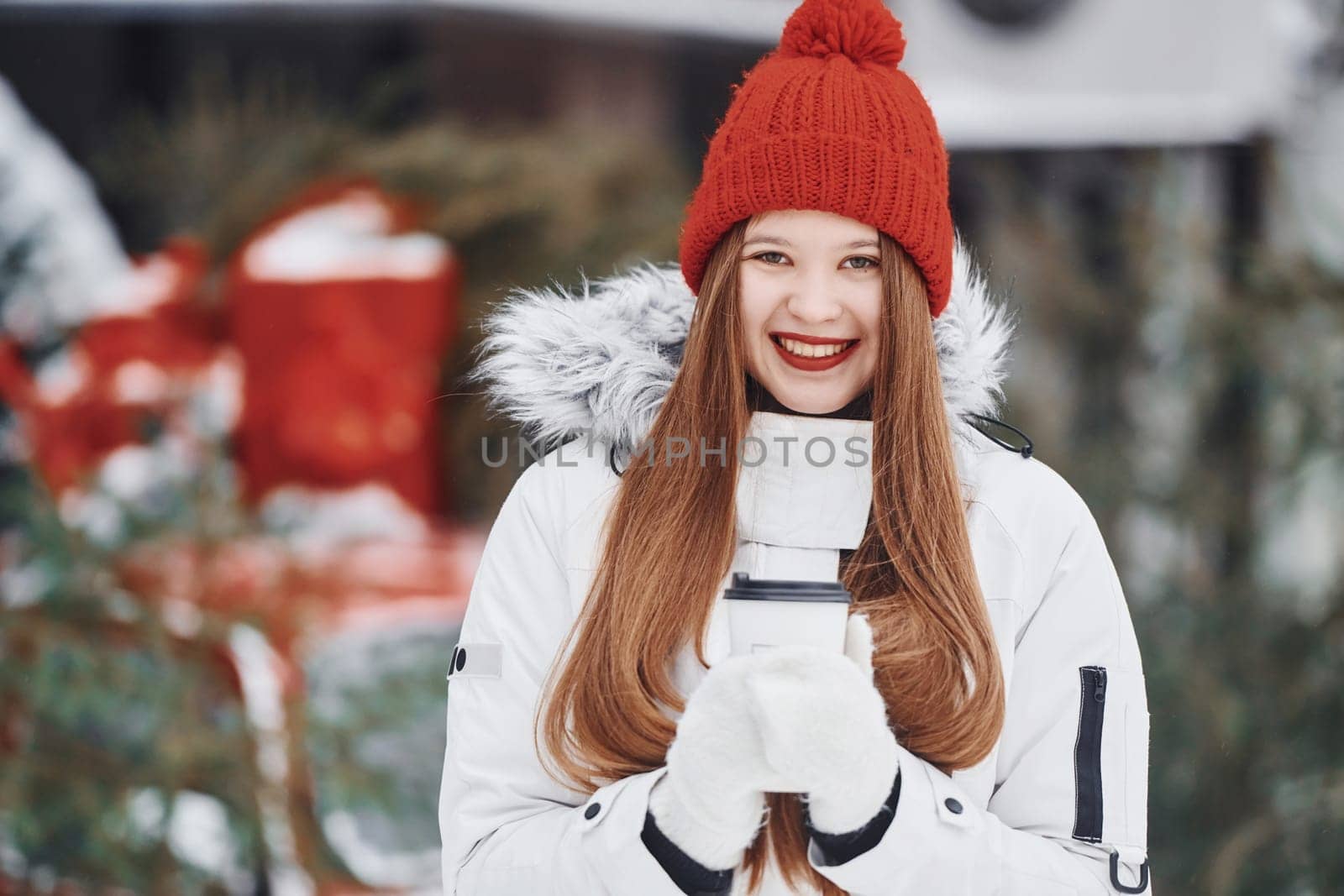 With cup of drink in hands. Happy young woman standing outdoors and celebrating christmas holidays.