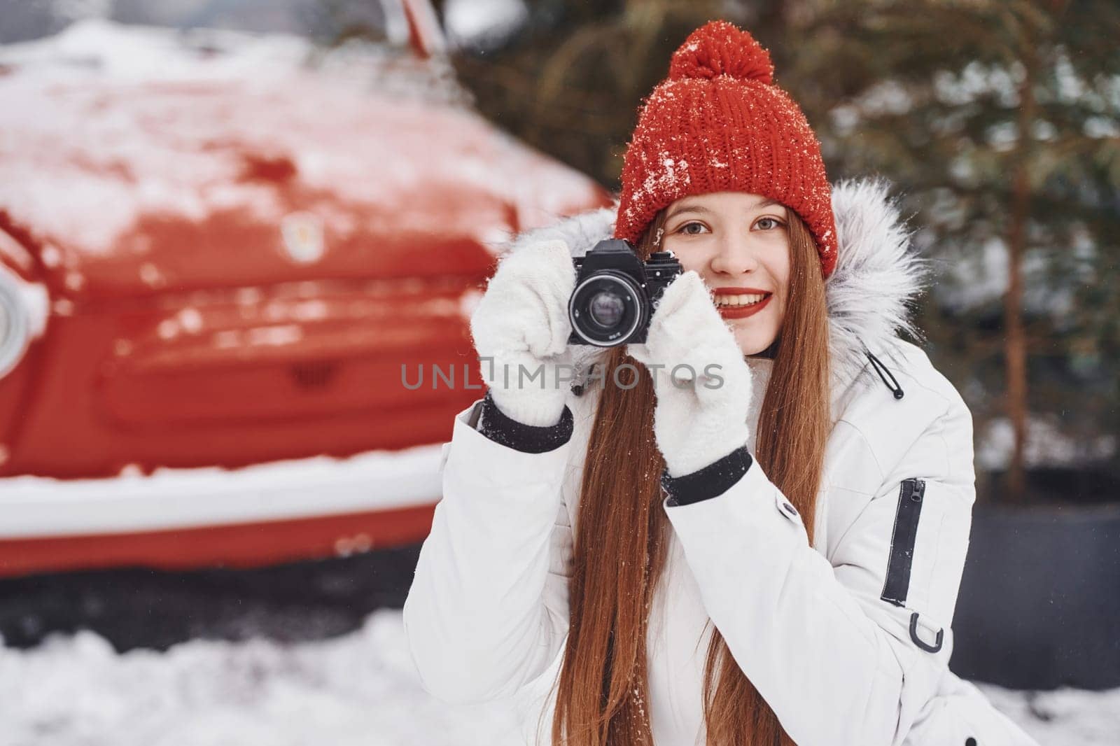 With camera in hands. Happy young woman standing outdoors and celebrating christmas holidays.
