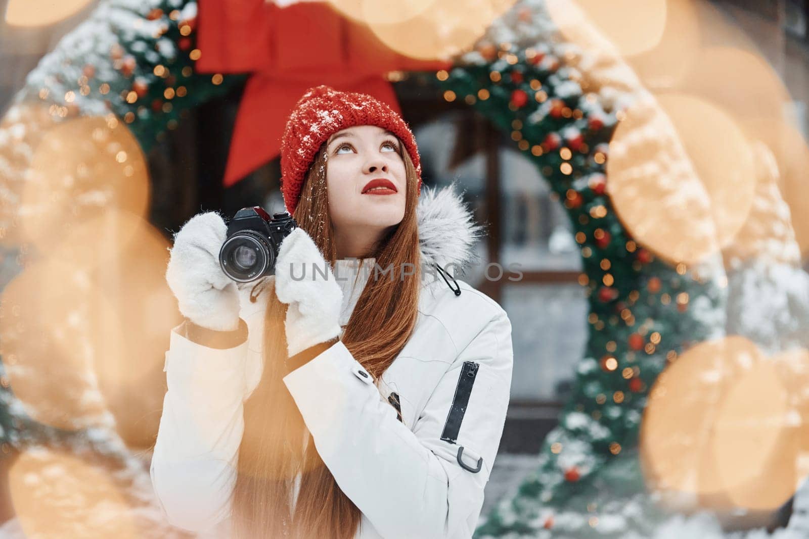 With camera in hands. Happy young woman standing outdoors and celebrating christmas holidays.