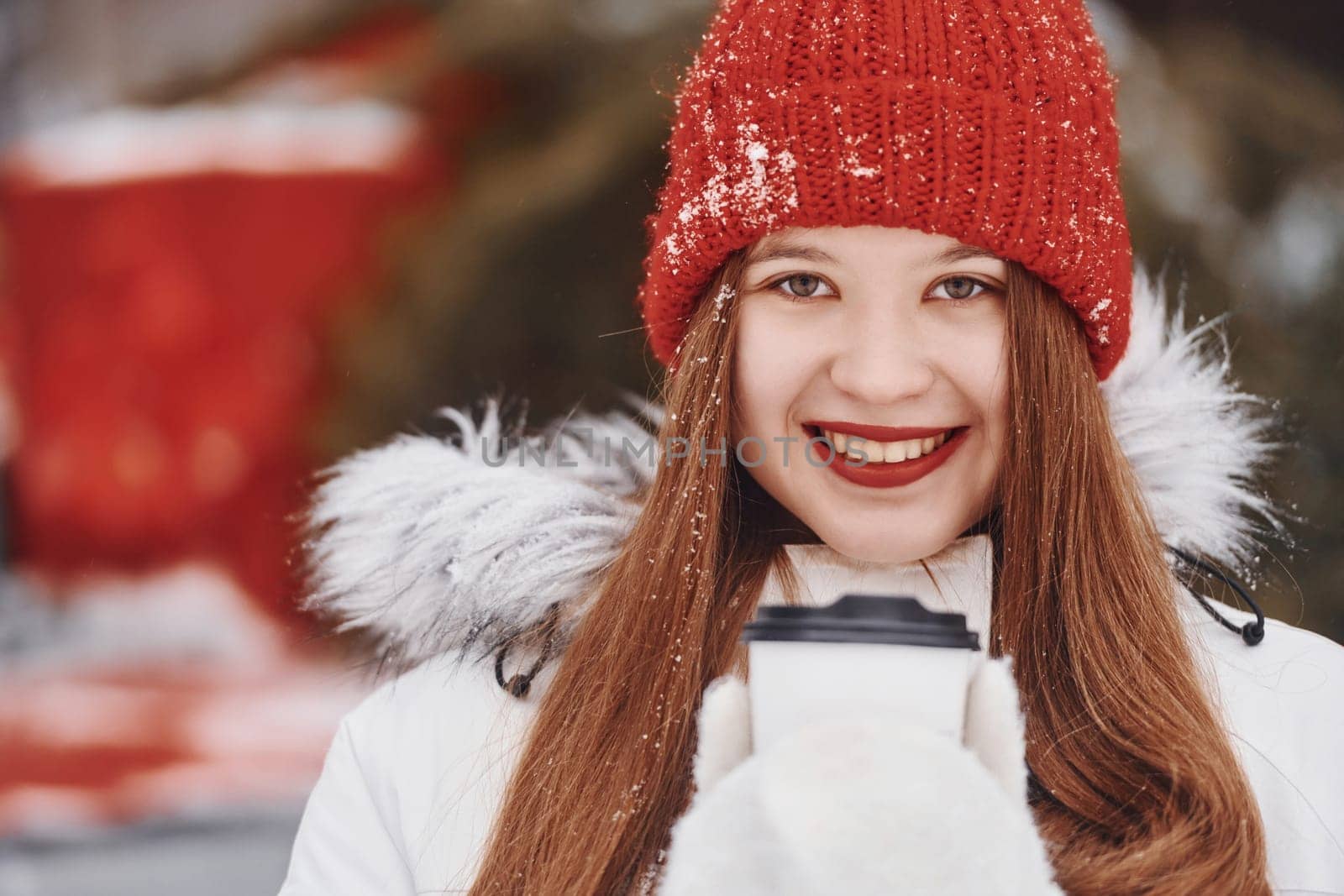 With cup of drink in hands. Happy young woman standing outdoors and celebrating christmas holidays.
