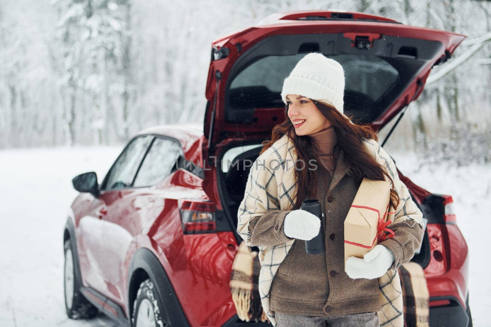 Sitting on the back of a car. Beautiful young woman is outdoors near her red automobile at winter time.