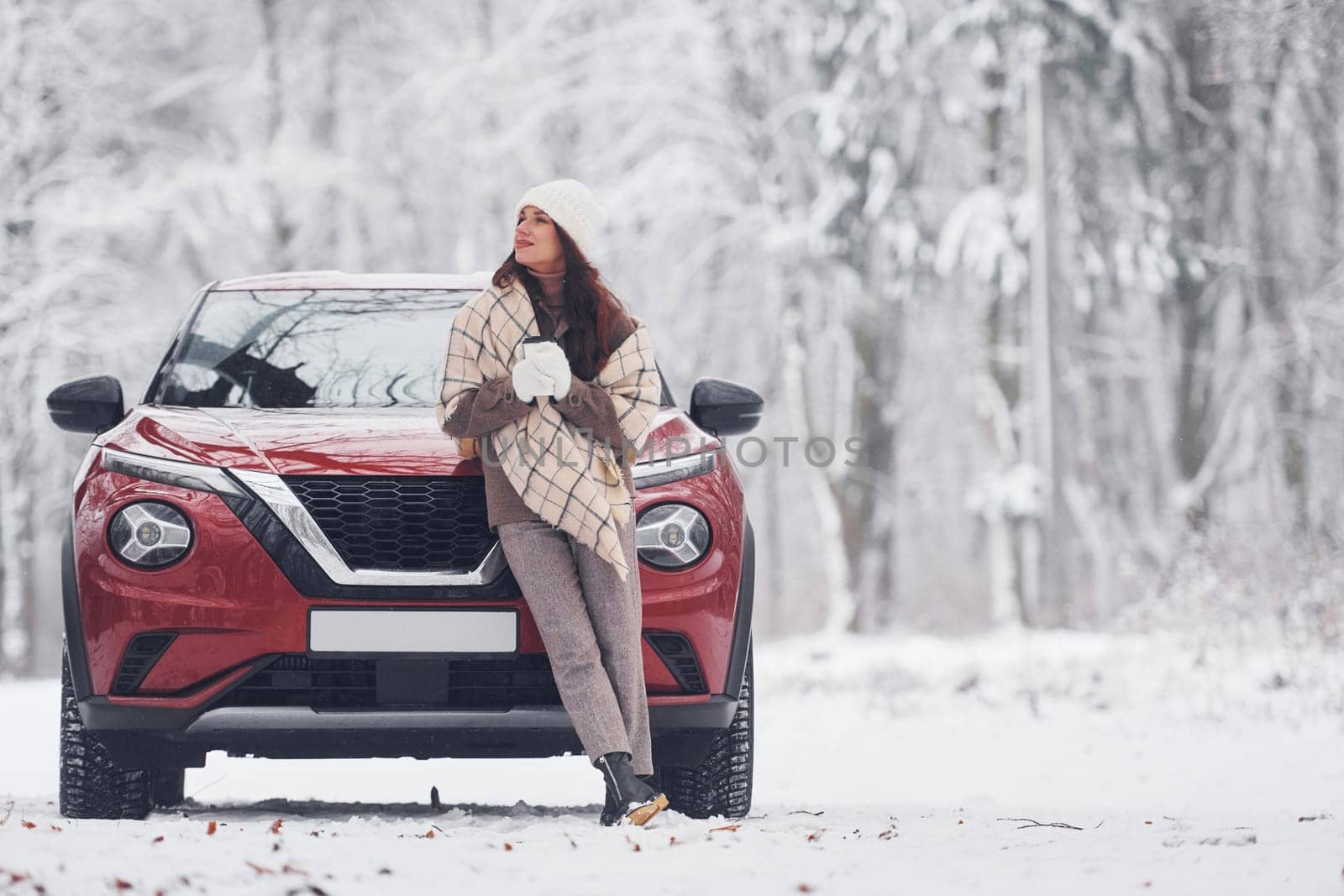 In front of her car. Beautiful young woman is outdoors near her red automobile at winter time.