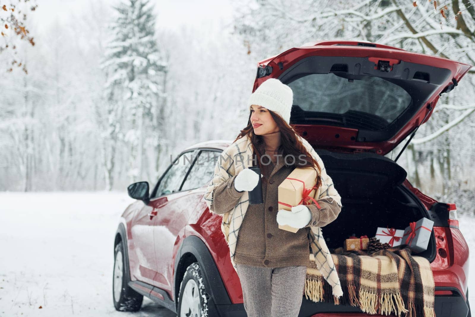 Sitting on the back of a car. Beautiful young woman is outdoors near her red automobile at winter time.