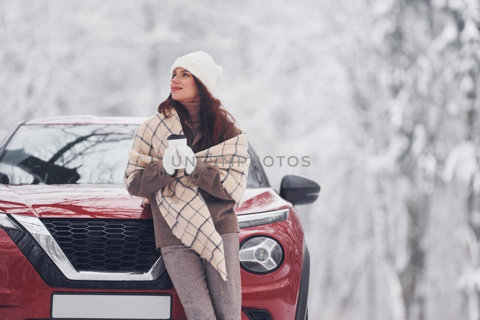 In front of her car. Beautiful young woman is outdoors near her red automobile at winter time.