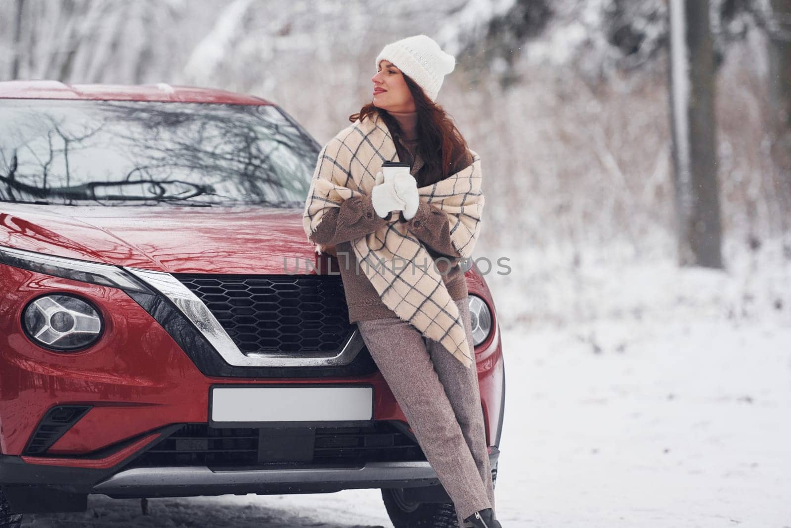 In front of her car. Beautiful young woman is outdoors near her red automobile at winter time.