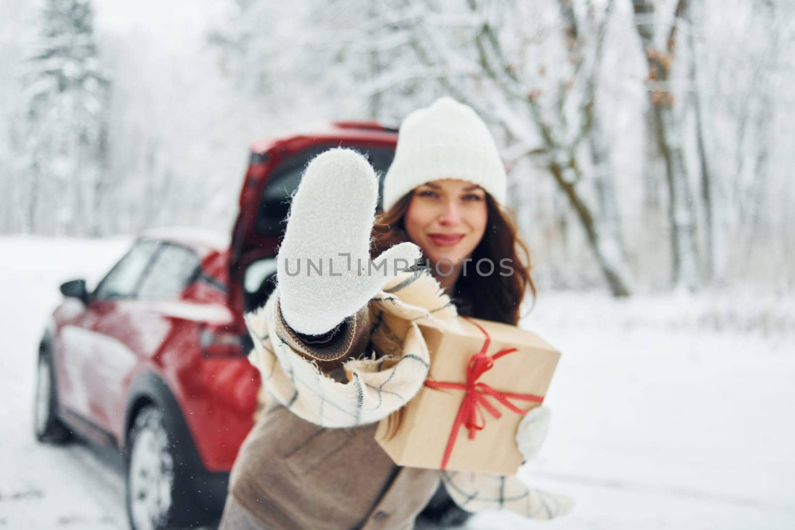 In front of her car. Beautiful young woman is outdoors near her red automobile at winter time.
