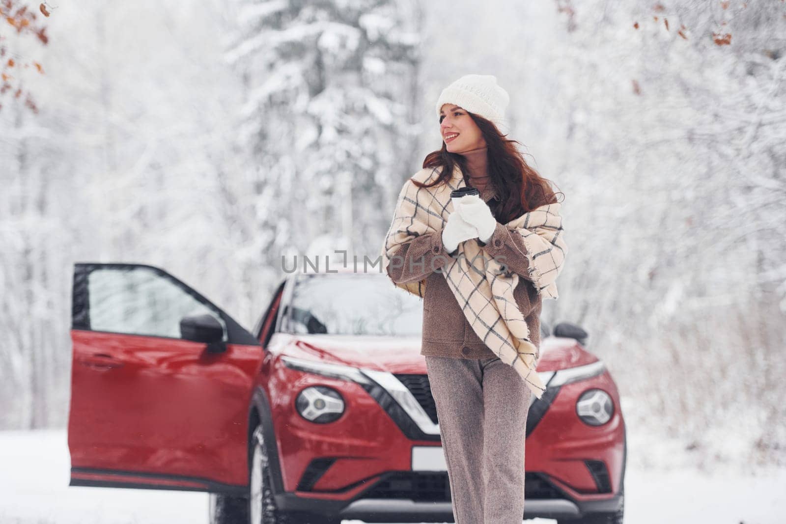 In the forest. Beautiful young woman is outdoors near her red automobile at winter time.