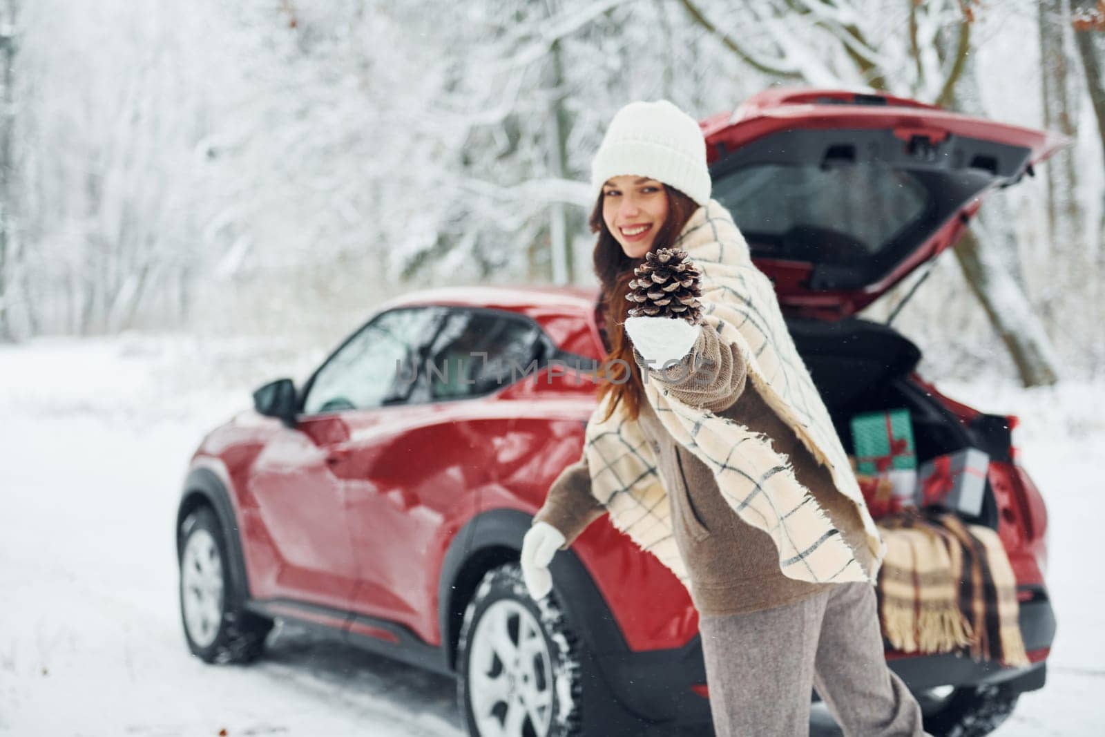 In the forest. Beautiful young woman is outdoors near her red automobile at winter time.