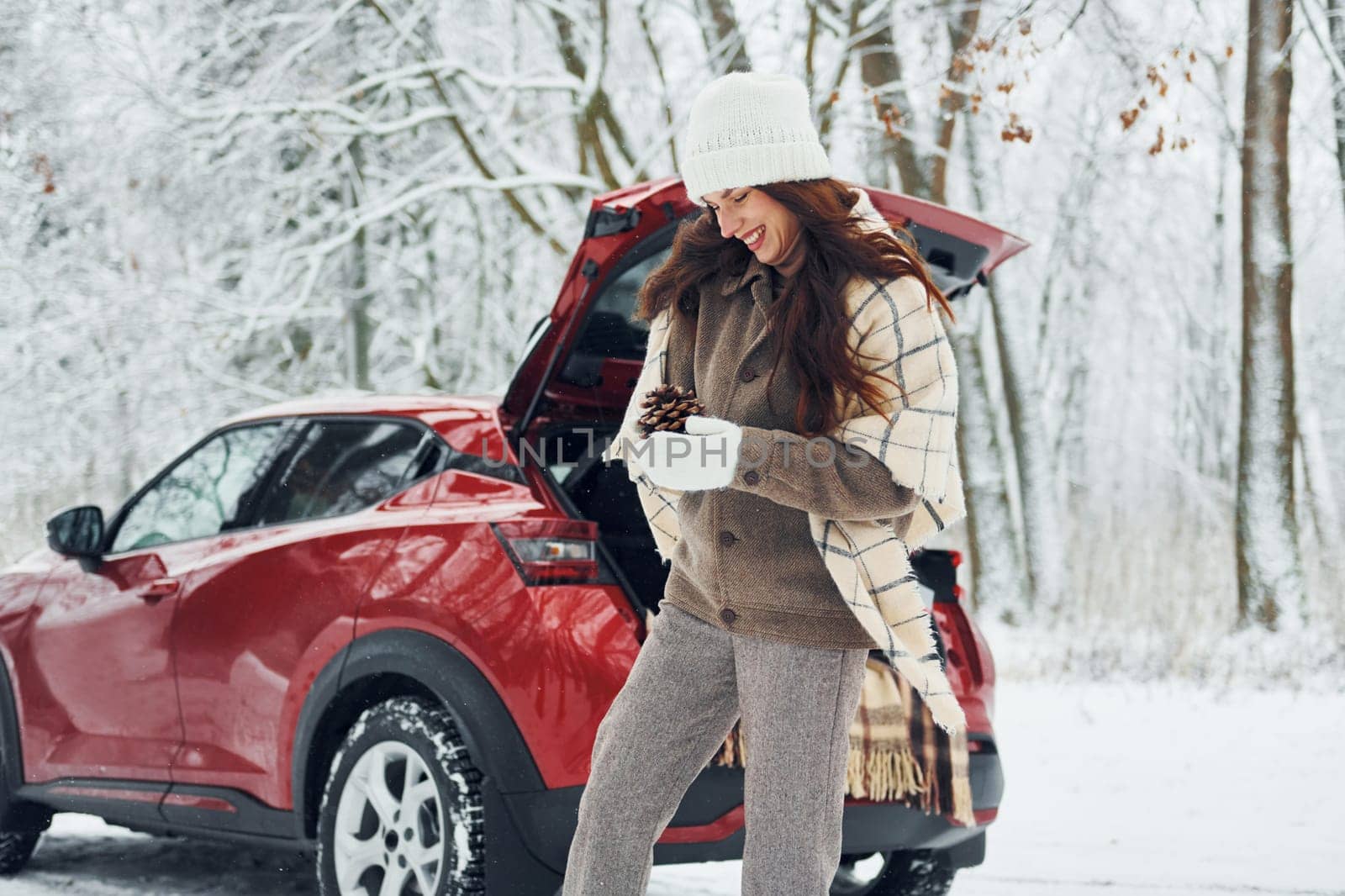 Cheerful emotions. Beautiful young woman is outdoors near her red automobile at winter time.