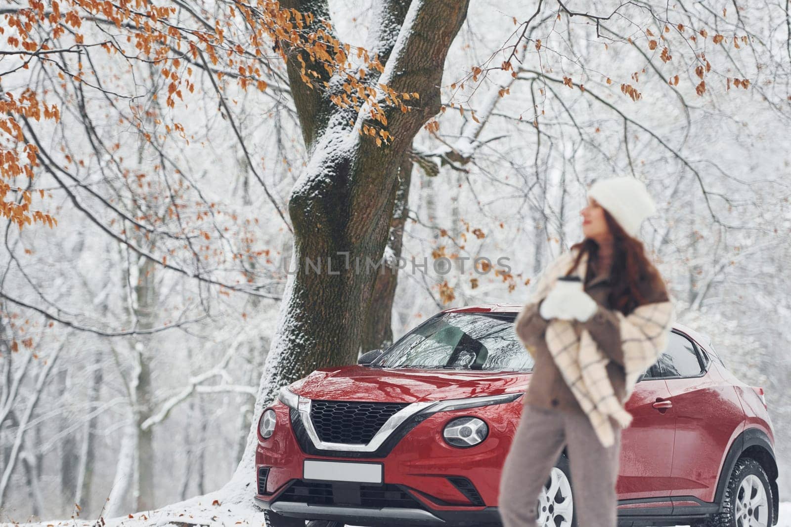 Rural scene. Beautiful young woman is outdoors near her red automobile at winter time.