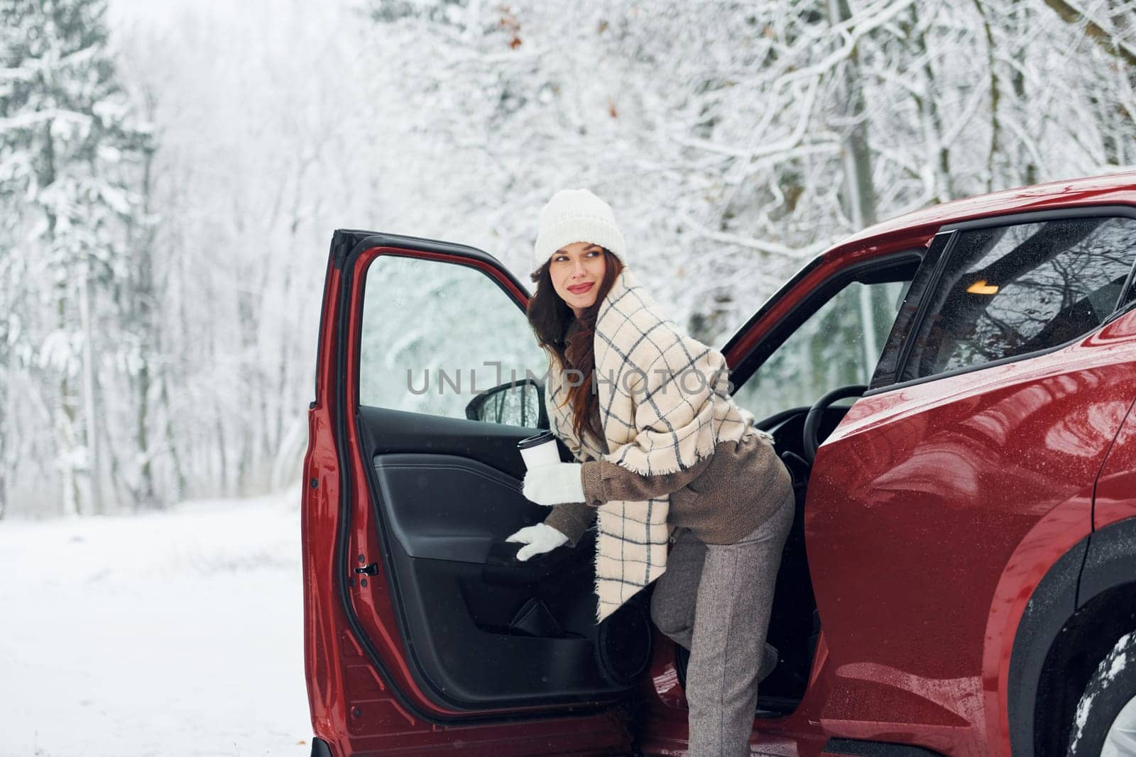 Positive emotions. Beautiful young woman is outdoors near her red automobile at winter time.