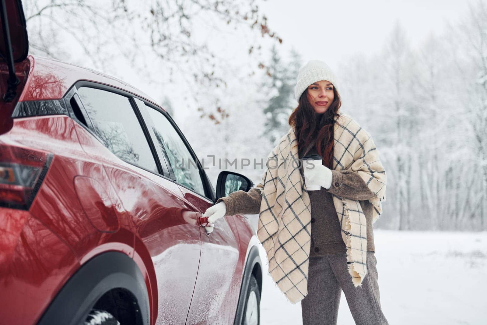 Positive emotions. Beautiful young woman is outdoors near her red automobile at winter time.