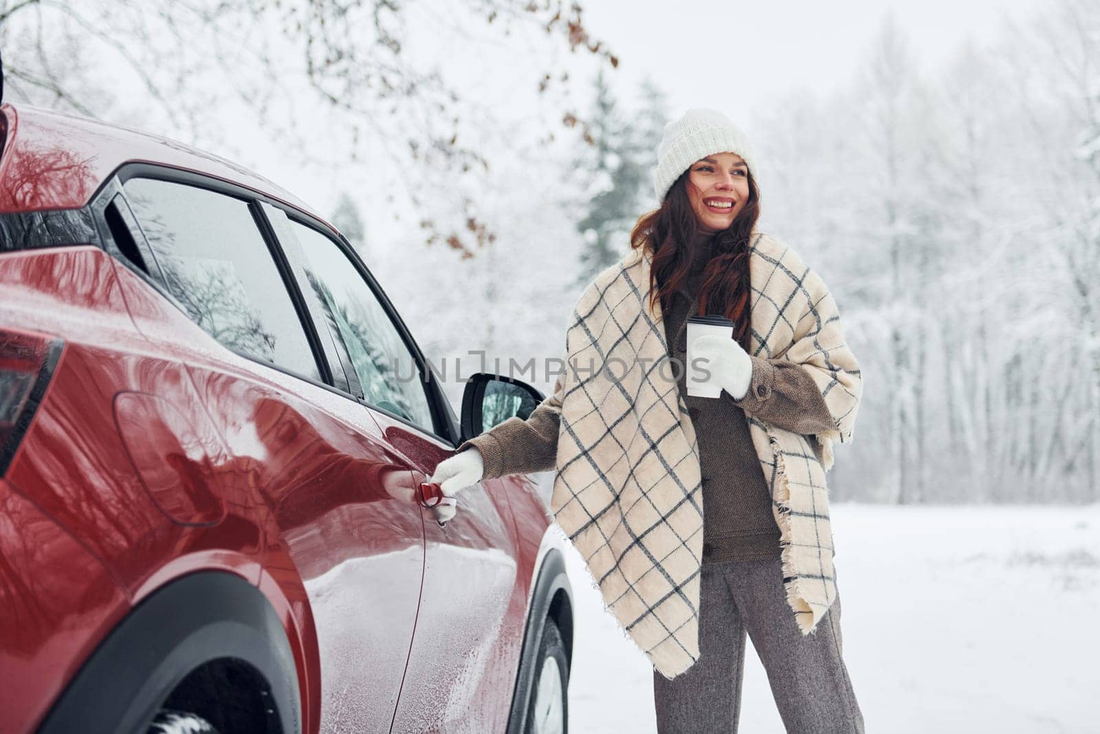 Positive emotions. Beautiful young woman is outdoors near her red automobile at winter time.