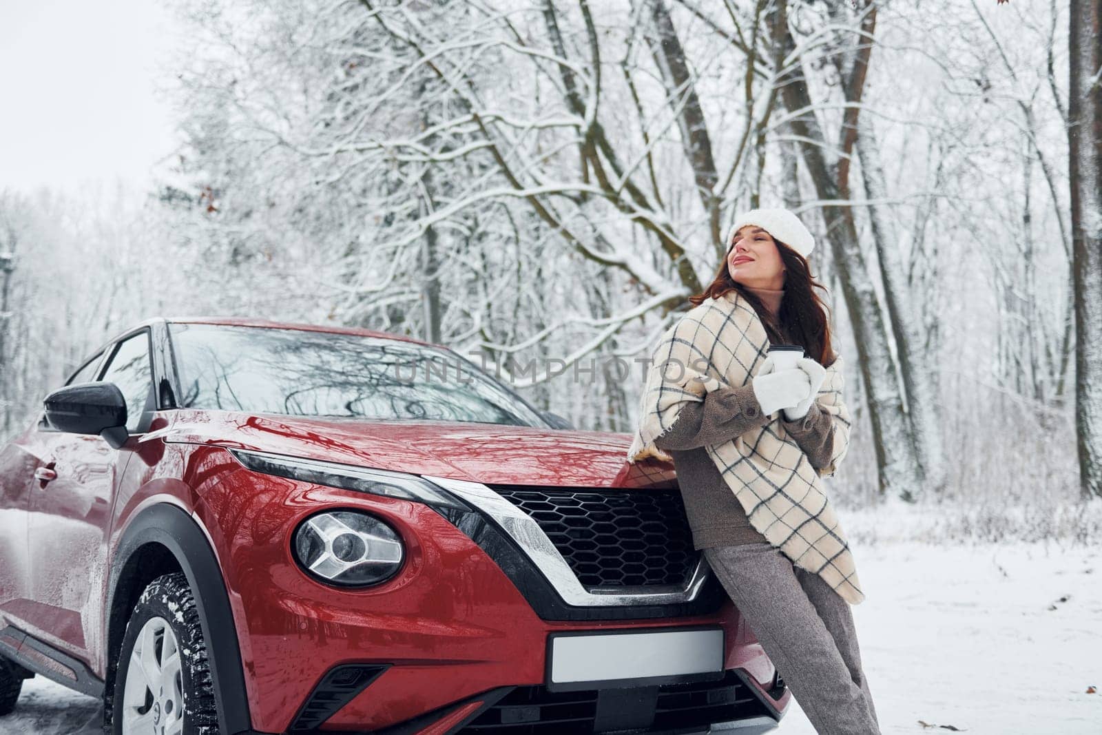 Beautiful winter background. Beautiful young woman is outdoors near her red automobile at winter time.