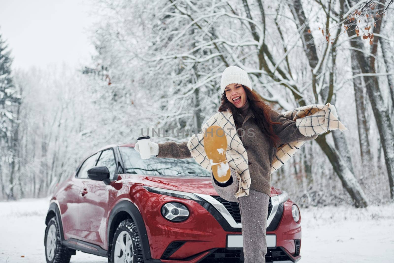 Beautiful winter background. Beautiful young woman is outdoors near her red automobile at winter time.