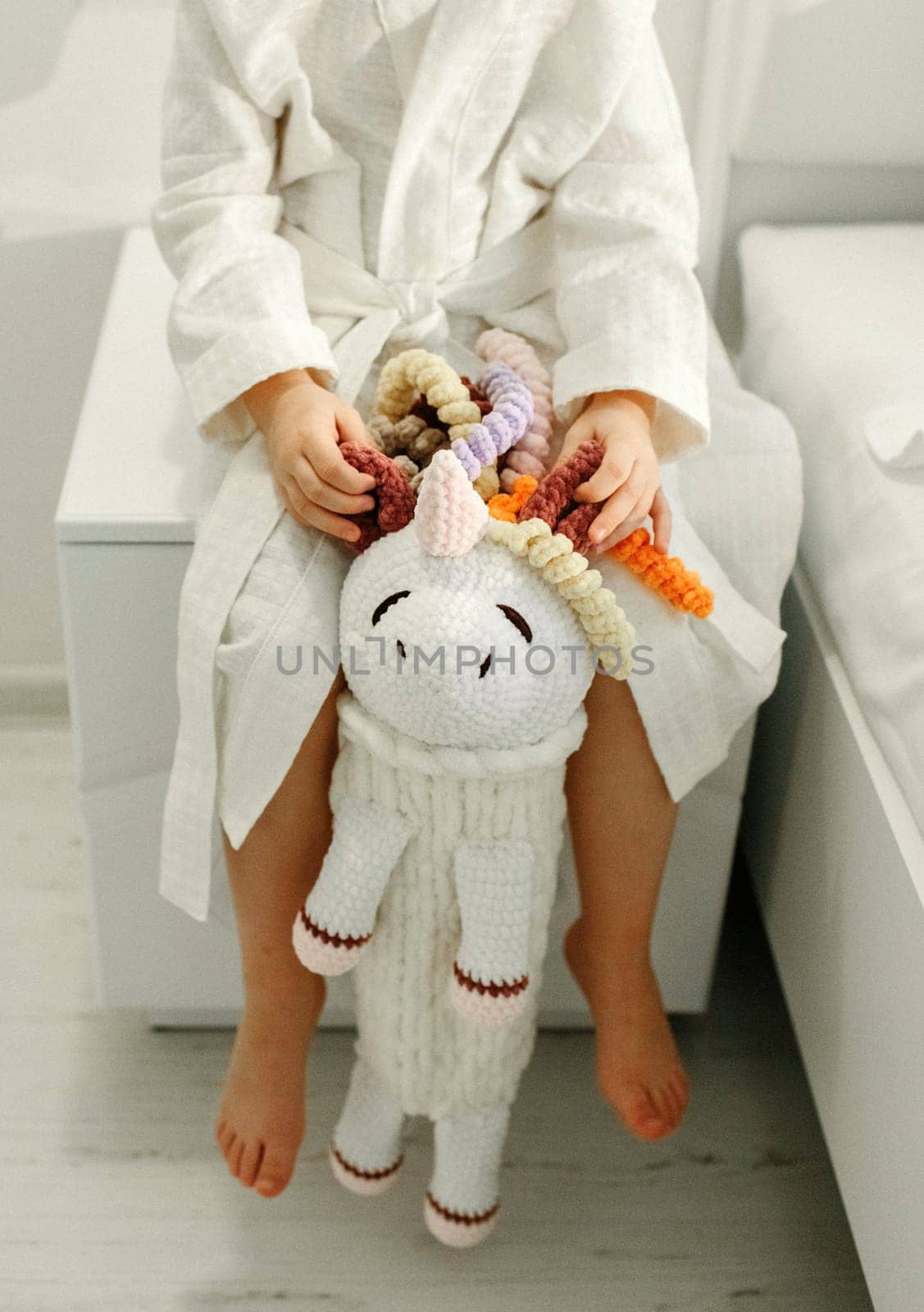 A girl in a bathrobe plays with a knitted unicorn.
