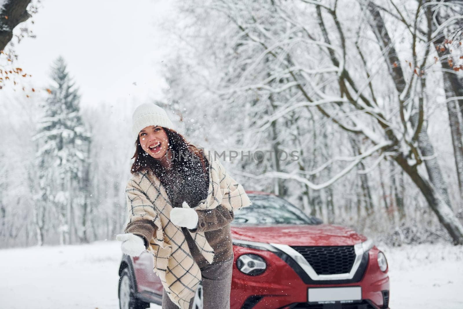 Beautiful nature. Young woman is outdoors near her red automobile at winter time.