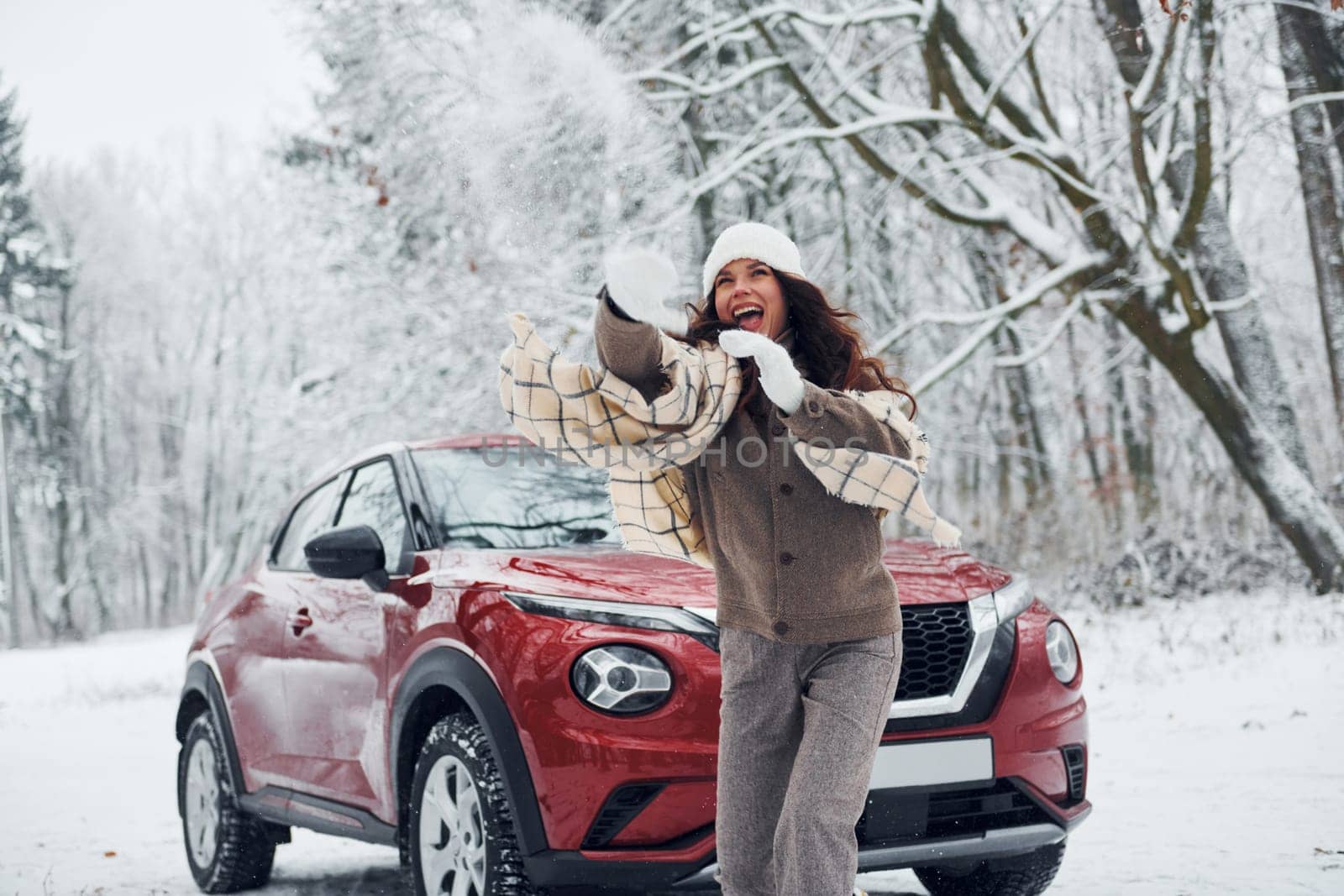 Beautiful nature. Young woman is outdoors near her red automobile at winter time.