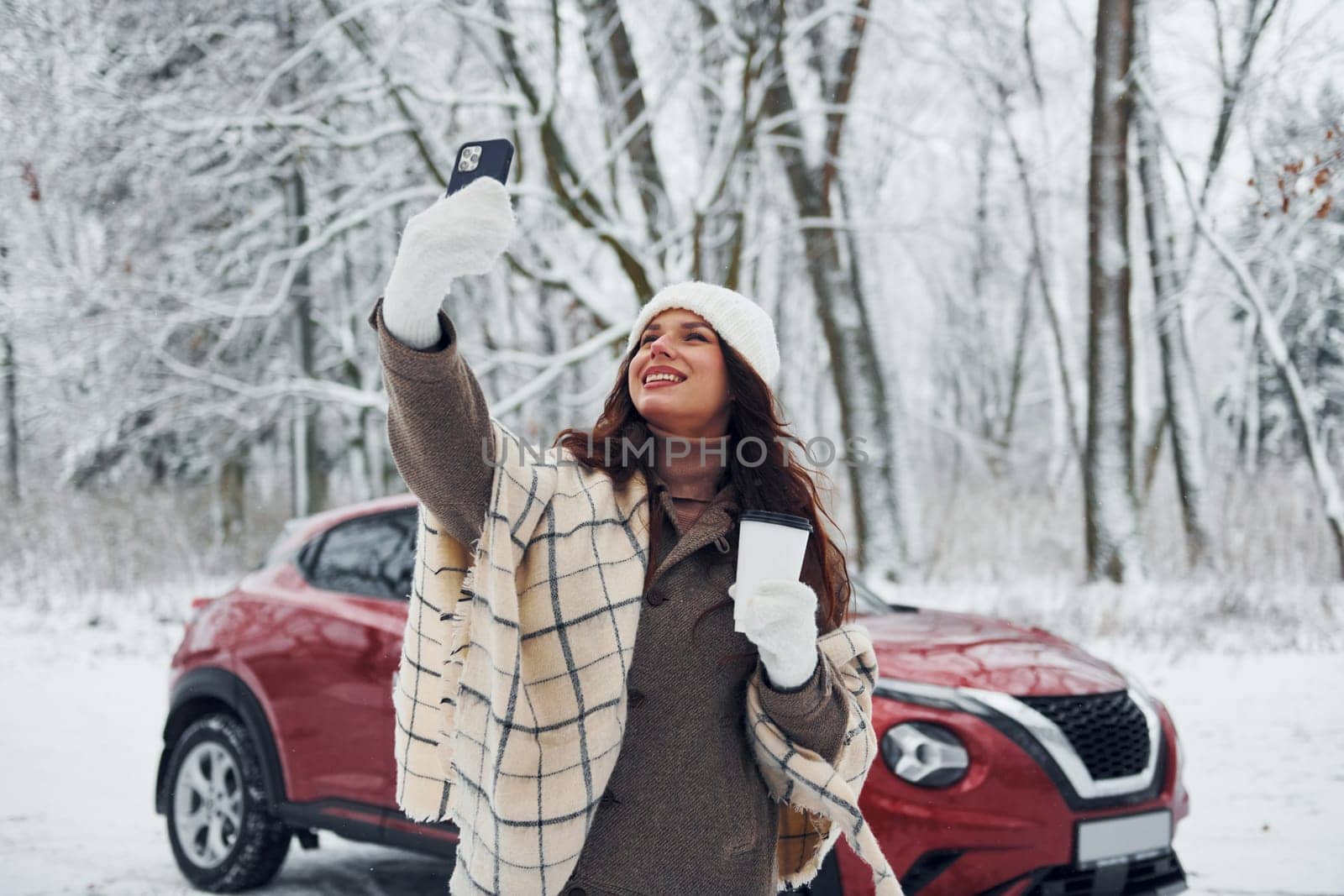 Beautiful nature. Young woman is outdoors near her red automobile at winter time.