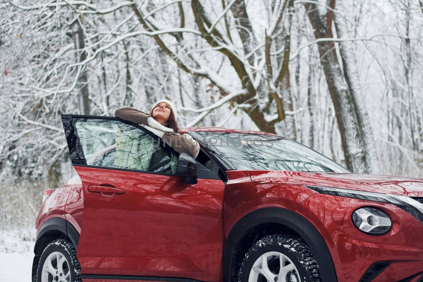 Walking out off car. Beautiful young woman is outdoors near her red automobile at winter time.