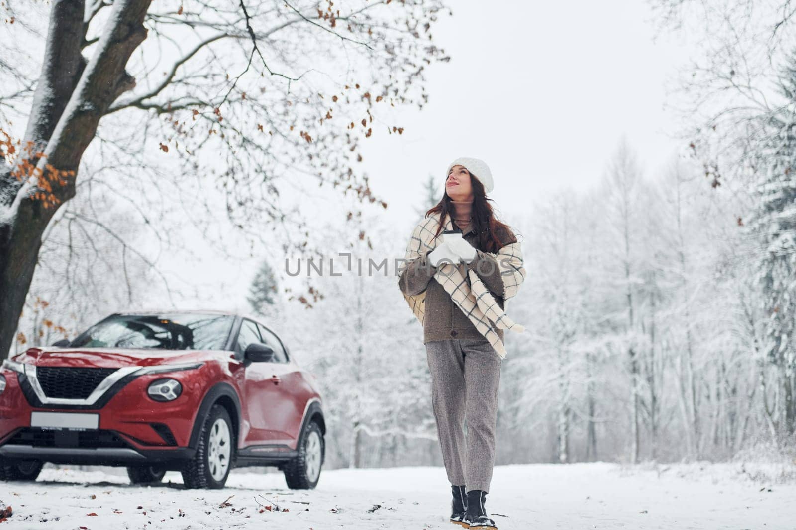 Non urban scene. Beautiful young woman is outdoors near her red automobile at winter time.