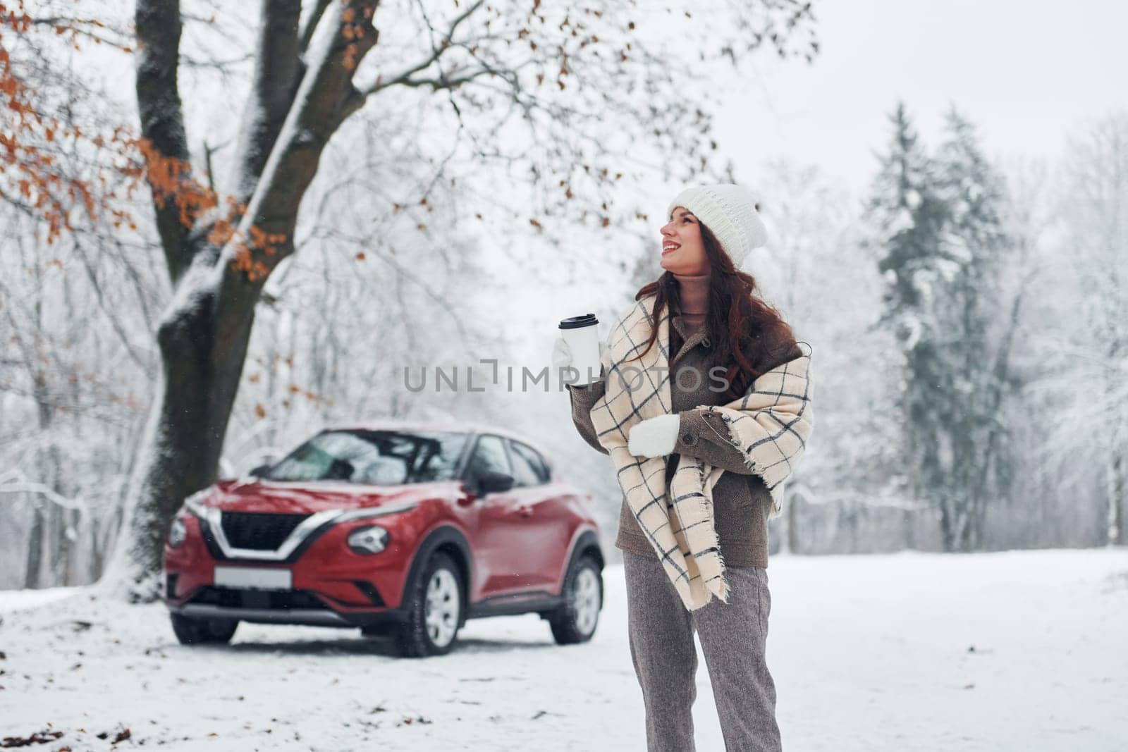 Non urban scene. Beautiful young woman is outdoors near her red automobile at winter time.