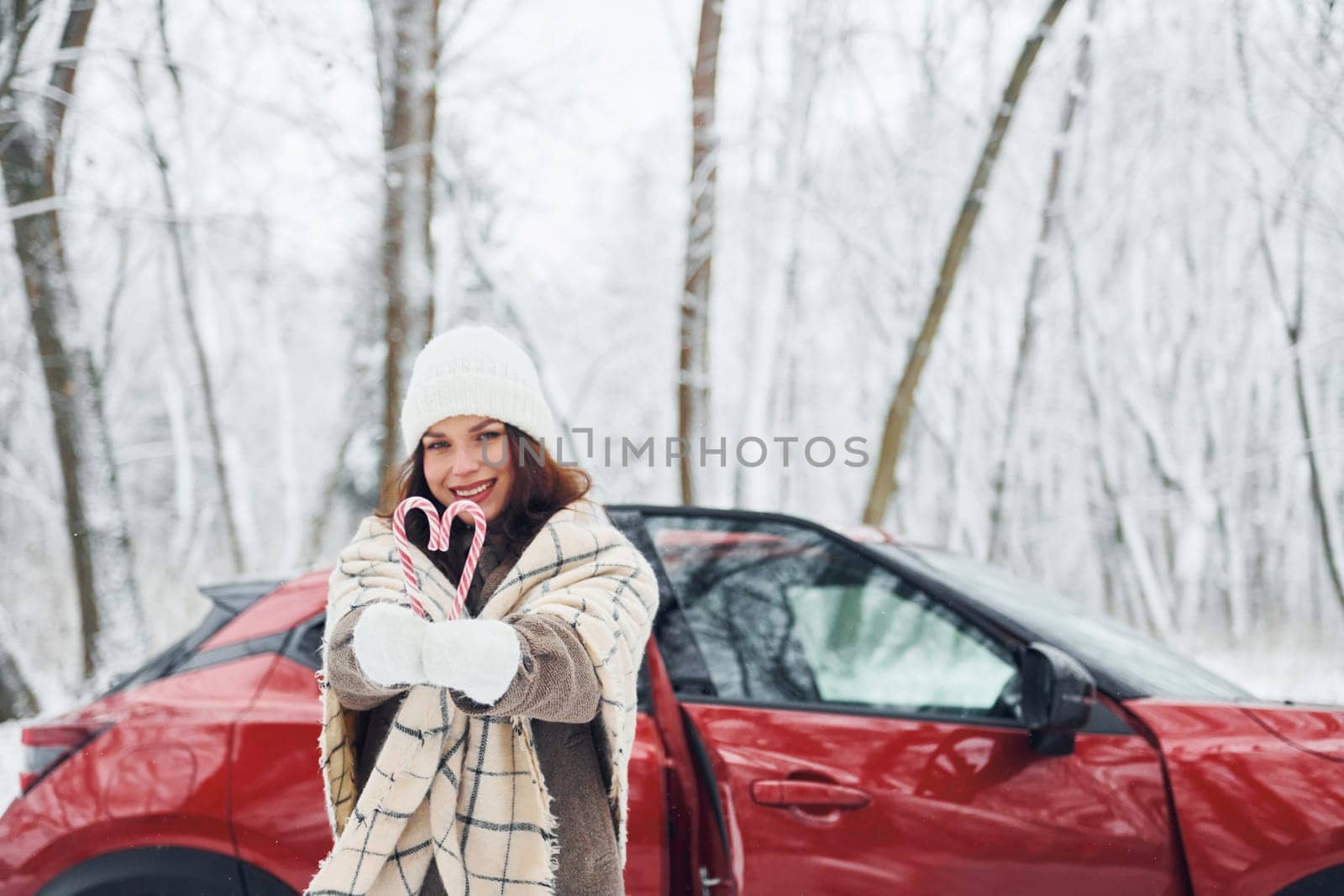 Non urban scene. Beautiful young woman is outdoors near her red automobile at winter time.