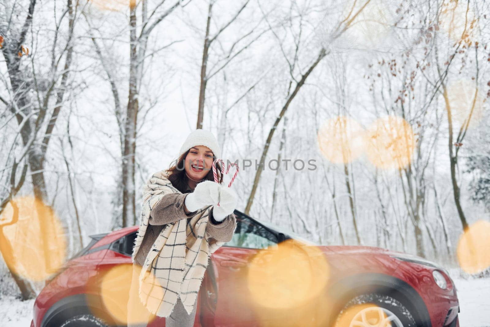 Non urban scene. Beautiful young woman is outdoors near her red automobile at winter time.