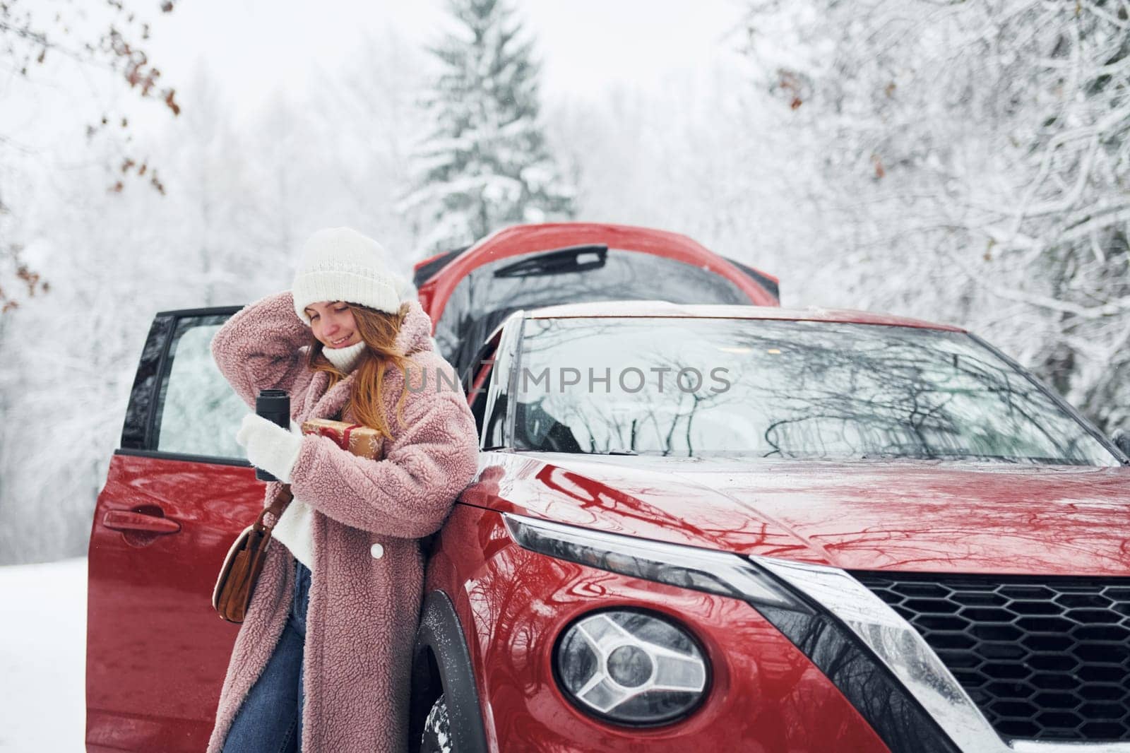 Having fun. Beautiful young woman is outdoors near her red automobile at winter time.