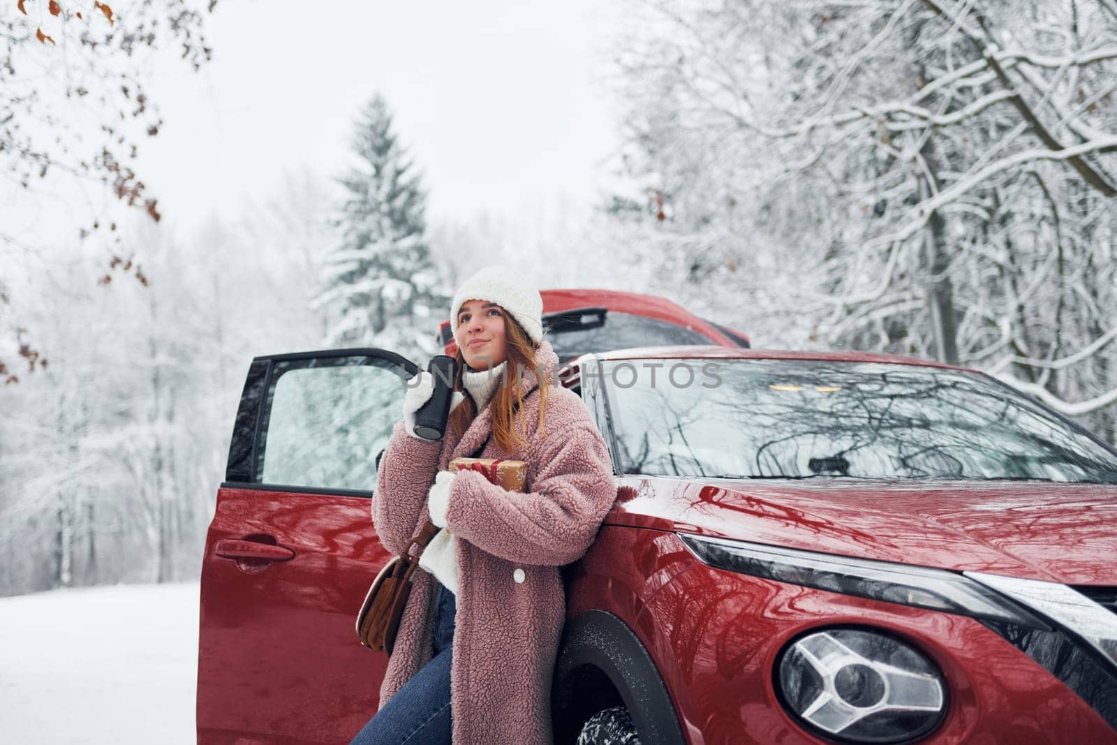 Having fun. Beautiful young woman is outdoors near her red automobile at winter time.