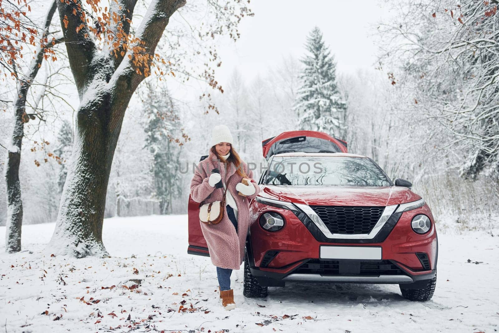 Having fun. Beautiful young woman is outdoors near her red automobile at winter time.