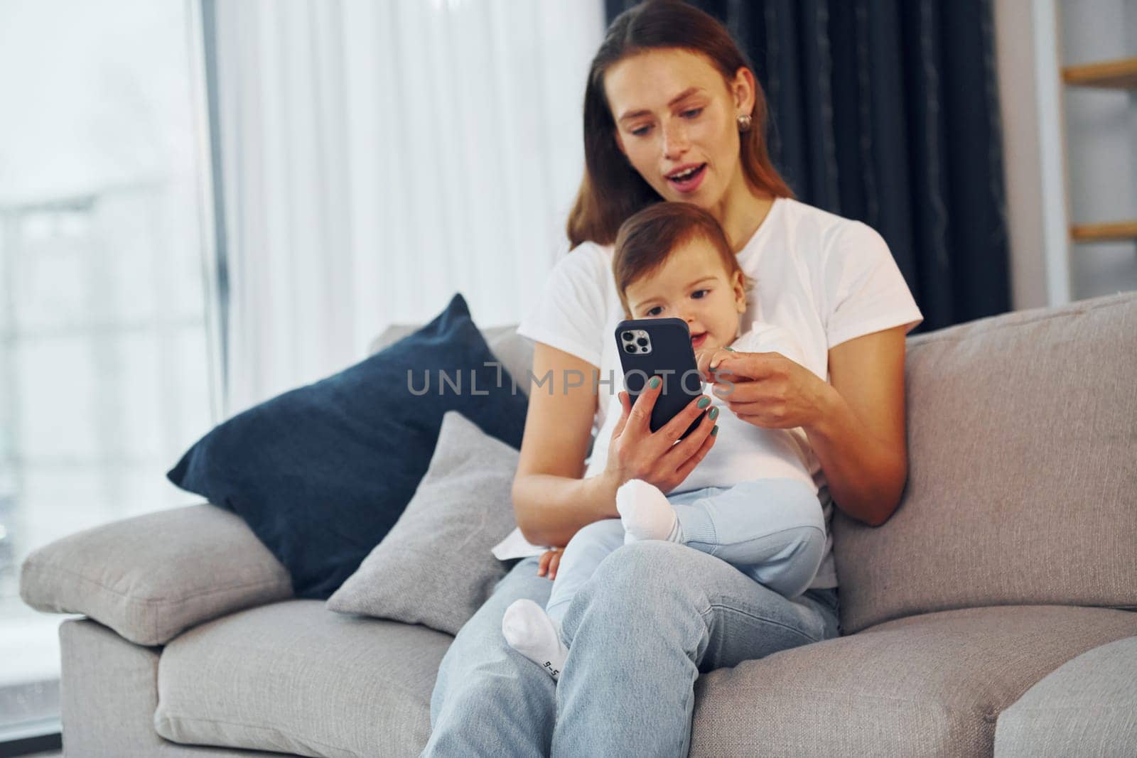 With smartphone in hand. Mother with her little daughter is at home together.