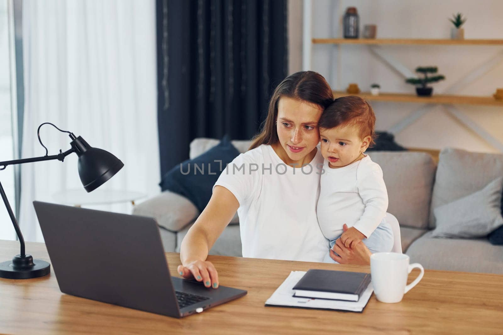 Using laptop. Mother with her little daughter is at home together.